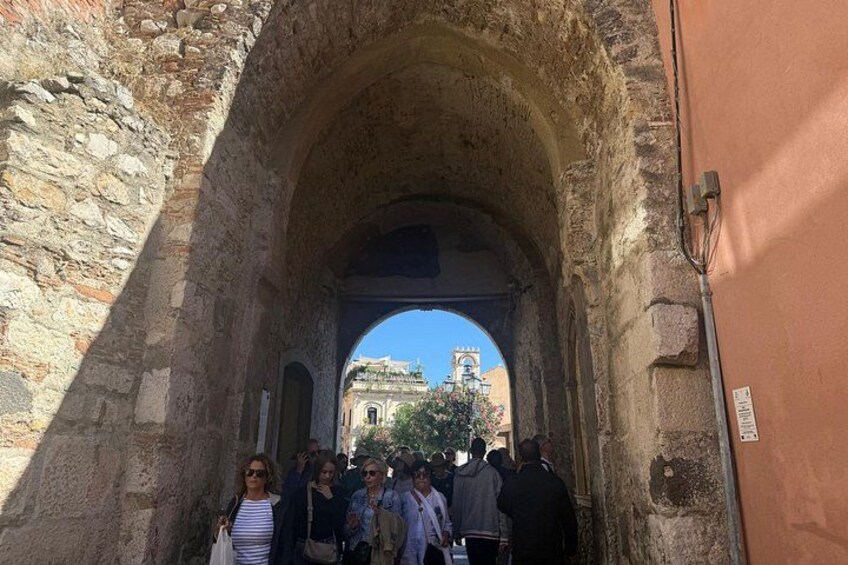 An ancient stone archway with tourists walking through it. 5