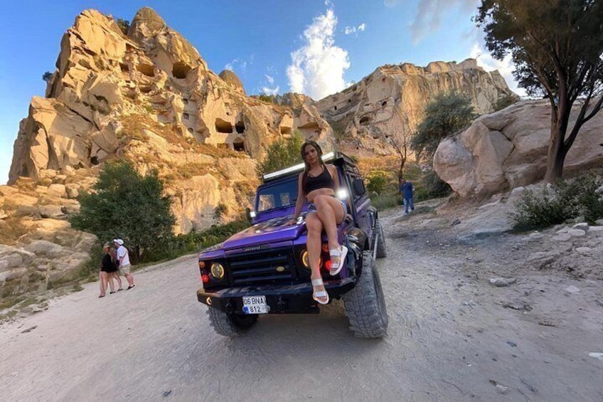 Un vehículo todoterreno morado sobre un camino de tierra, con acantilados rocosos al fondo. 3