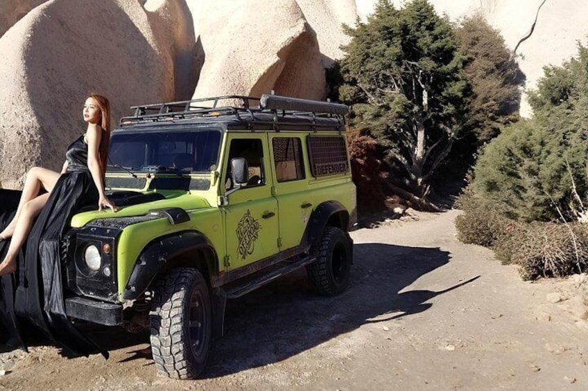 Un vehículo todoterreno verde estacionado en un camino de tierra con rocas grandes y árboles de fondo. 2