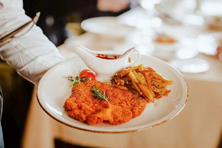 A person holding a plate with a breaded cutlet, fries, and a small bowl of sauce. 5