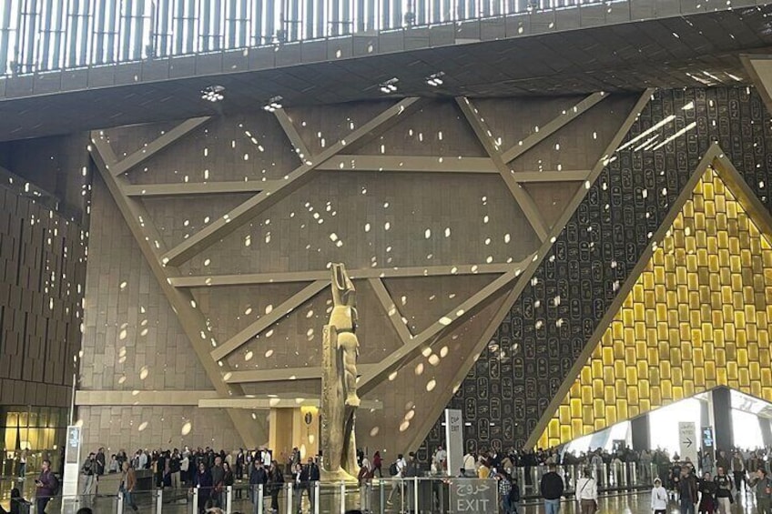 A large crowd gathered under a modern architectural structure with a prominent golden pattern and a statue. 4