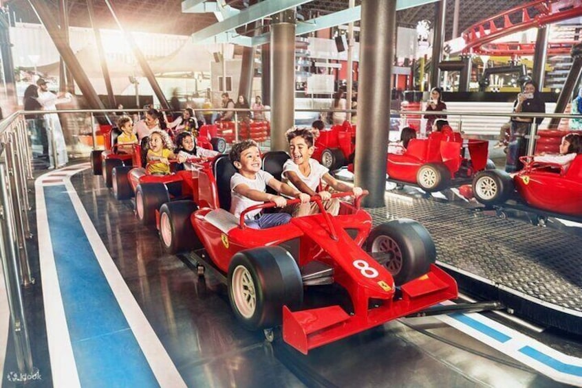 Niños en autos de carrera rojos en una pista dentro de un parque de atracciones cubierto. 3