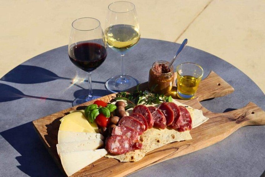 Eine Platte mit verschiedenen Wurstwaren, Käse und Oliven auf einem Holzbrett, begleitet von Weingläsern und einer Saucenschale. 2