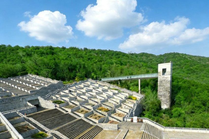 A large amphitheater with tiered seating, surrounded by lush green hills. 2