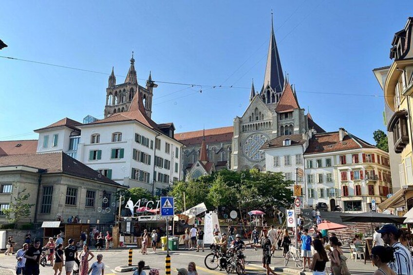 A bustling square with historic buildings, a prominent church with a tall spire, and a clock tower. 2