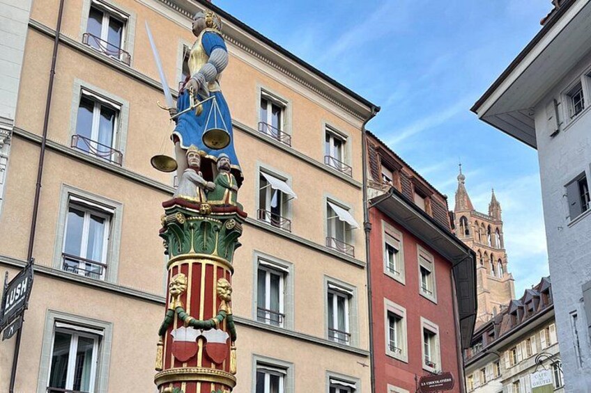 A colorful statue of a figure holding a sword and scales, set against a backdrop of historic buildings and a church tower. 4