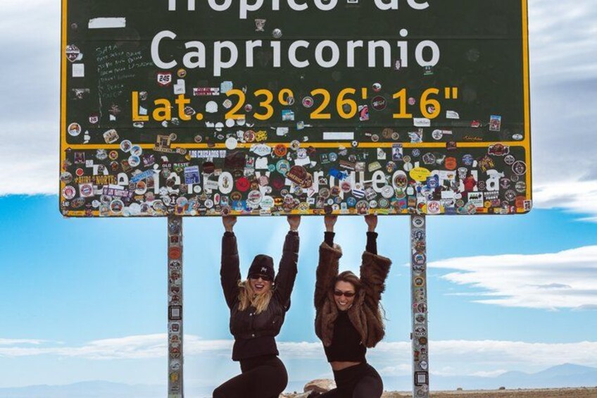 A sign with latitude and longitude coordinates, surrounded by various stickers. 3