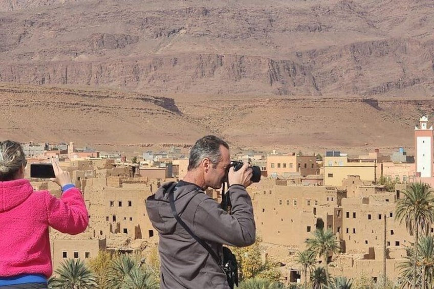 En person fotograferer et ørkenlandskab med bygninger og et bjerg i baggrunden. 5