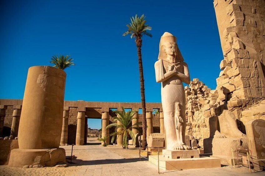 Un templo egipcio antiguo con una estatua grande, palmeras y columnas de piedra. 3