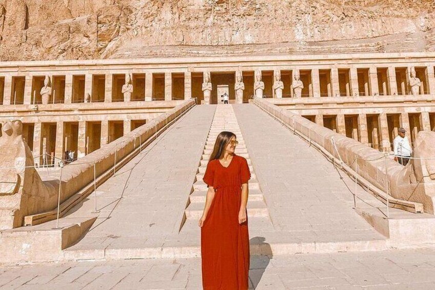 Una persona con un vestido rojo parada frente a un gran templo egipcio antiguo con una escalera monumental. 2