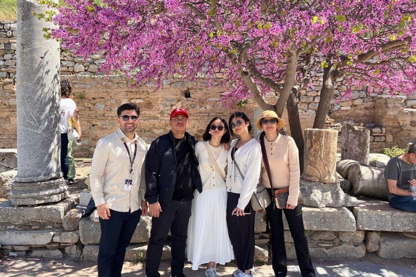 A group of people standing in front of ancient ruins with pink flowering trees. 2