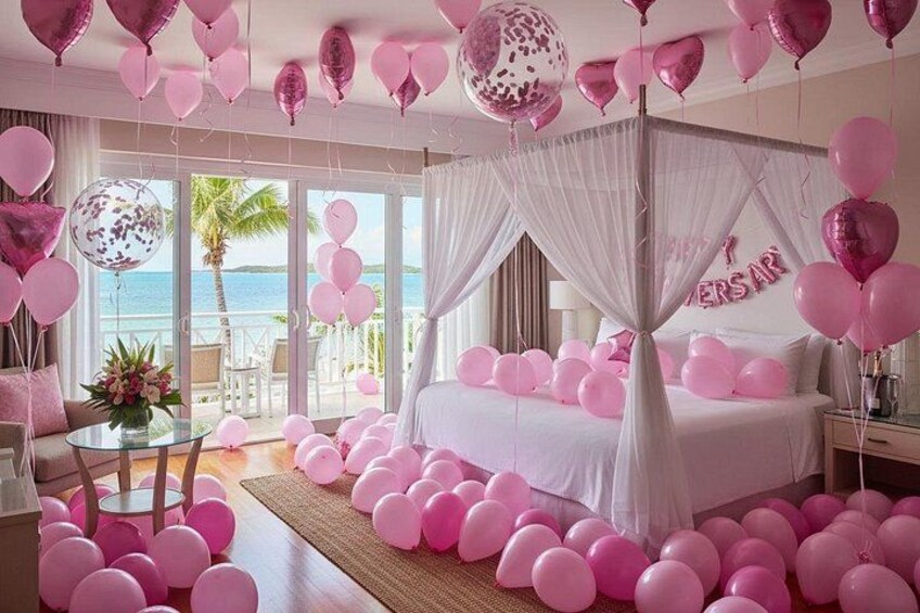 Ein in Rosa gehaltenes Schlafzimmer mit Bett, Luftballons und einem Balkon mit Blick aufs Meer. 1