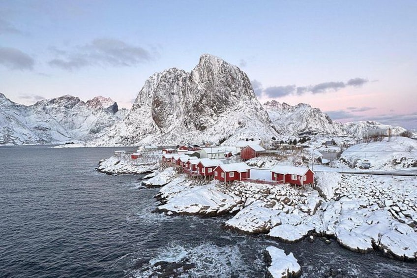 A coastal village with red buildings, a fjord, and snow-covered mountains. 3