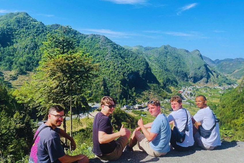 Eine Gruppe von Menschen sitzt am Straßenrand, im Hintergrund eine gebirgige Landschaft. 4