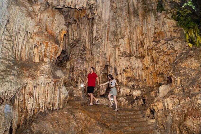 Two people walking on a rocky path in a cave with stalactites. 3