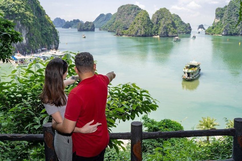 A couple overlooking a calm river with boats, surrounded by lush greenery and rocky hills. 5