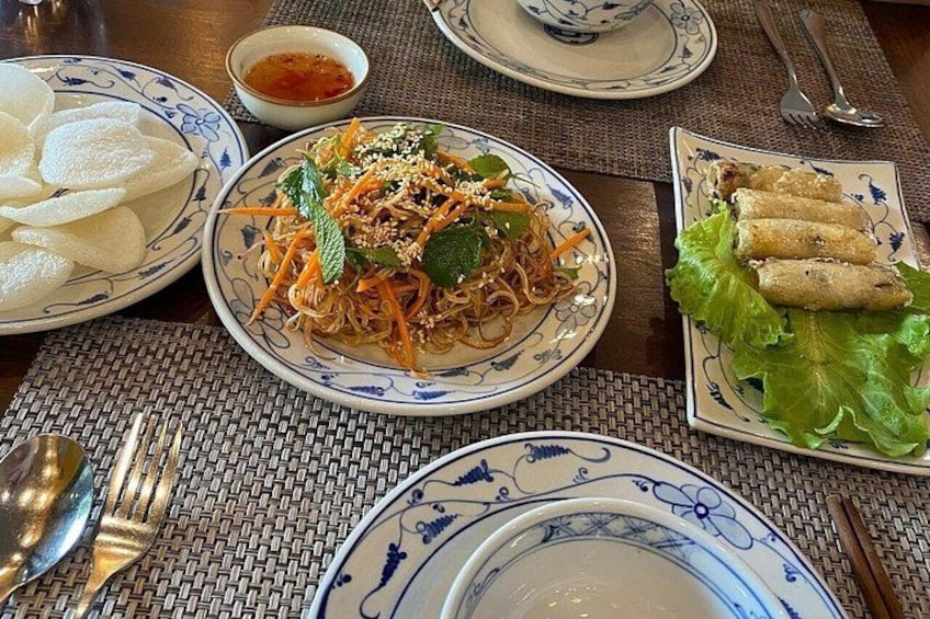 A table with various dishes including noodles, spring rolls, and a bowl of soup. 4