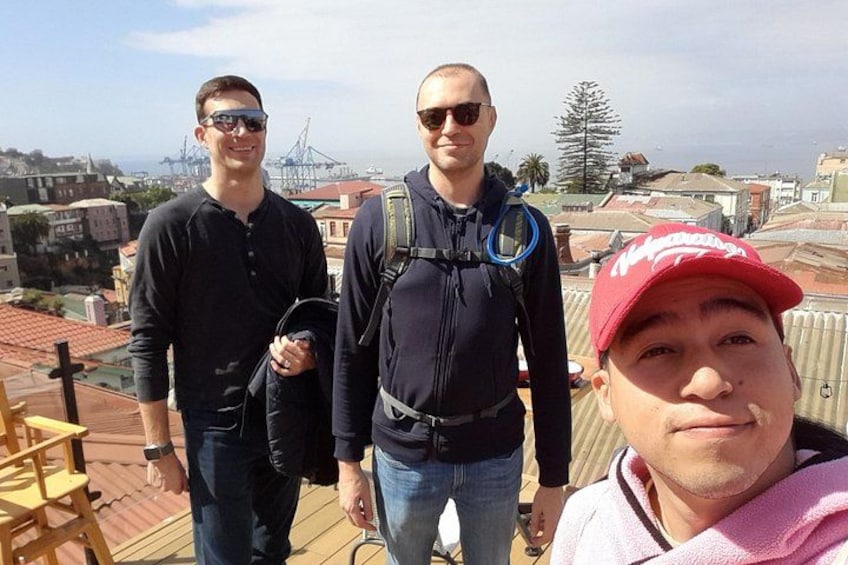 Three people standing on a rooftop with a cityscape in the background. 3