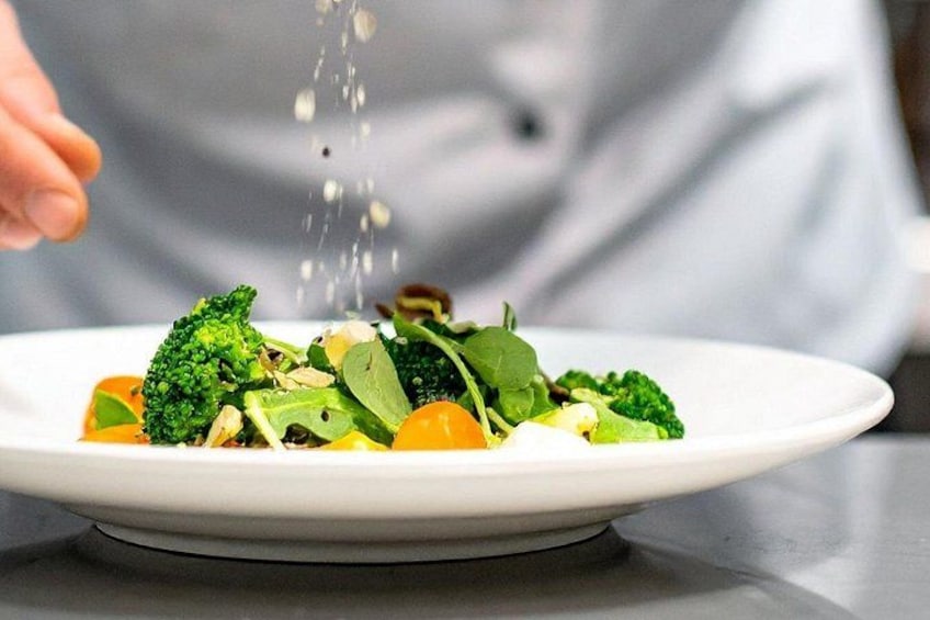 A plate of food with broccoli and other vegetables, being sprinkled with seasoning. 2