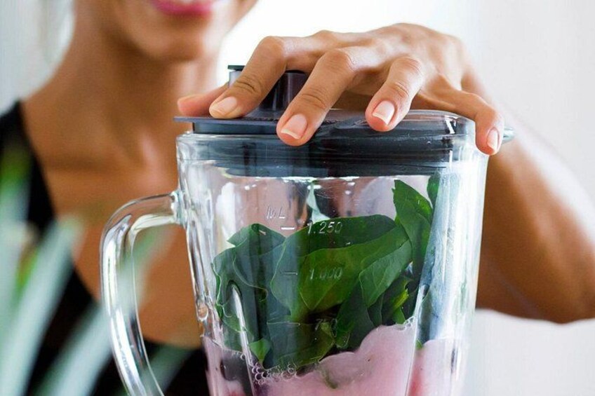 A hand holding a blender with a clear container, containing green leaves and a pink substance. 4