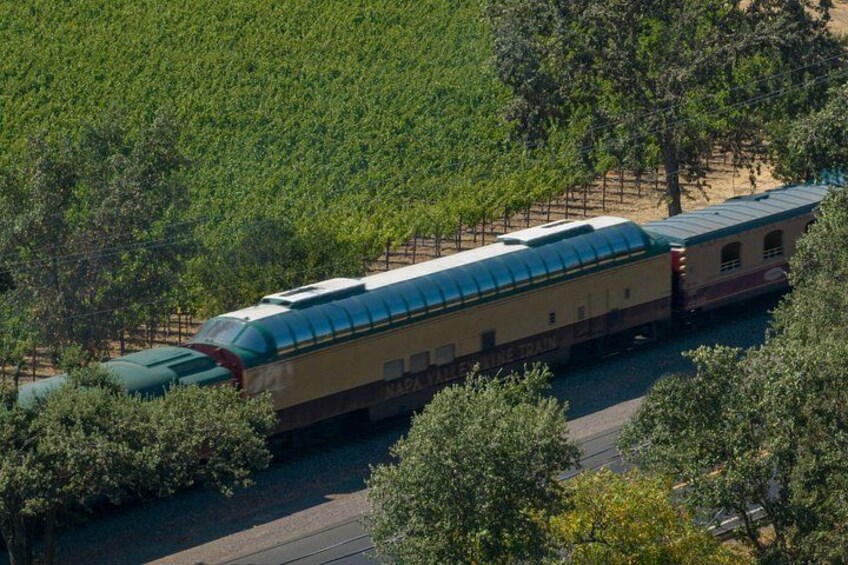 A train with a green roof and beige body traveling through a vineyard. 2