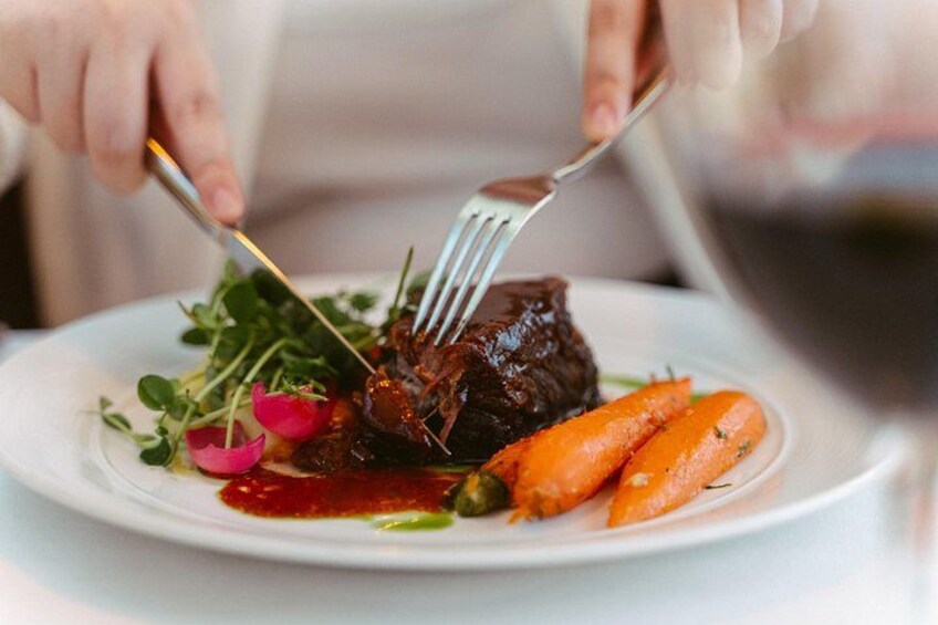 A person cutting a steak with a fork and knife on a plate with vegetables. 3