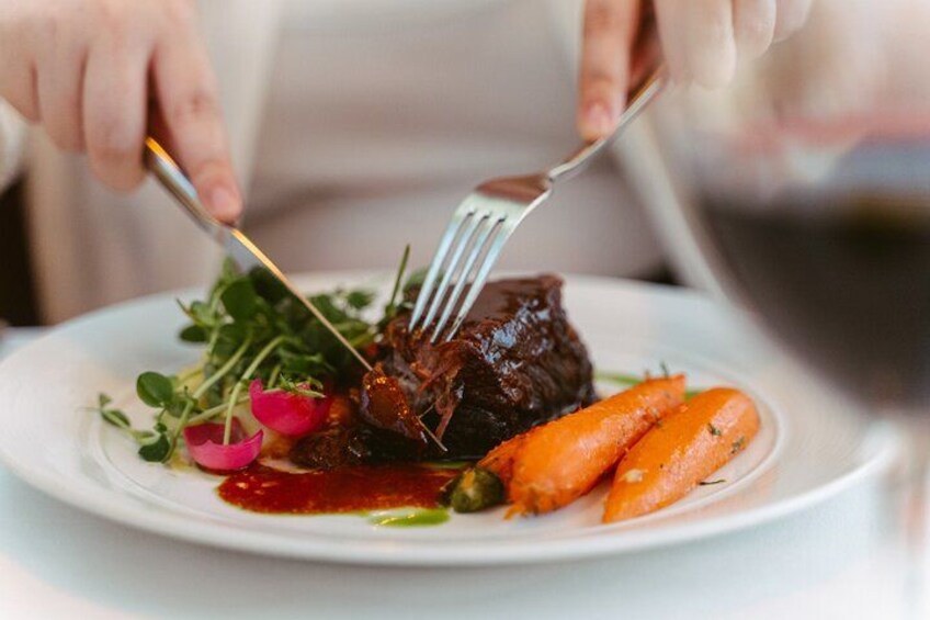 A person cutting a steak with a fork and knife on a plate with vegetables. 2