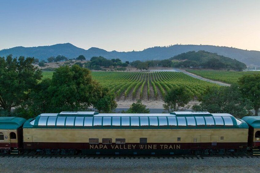 A train labeled 'Napa Valley Wine Train' on tracks with vineyards in the background. 1
