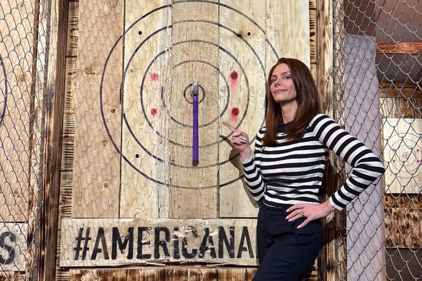 Una persona de pie frente a una tabla de madera con un dardo y el hashtag #AMERICA. 2