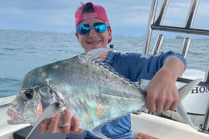 A person holding a large fish on a boat with the ocean and a distant island in the background. 3