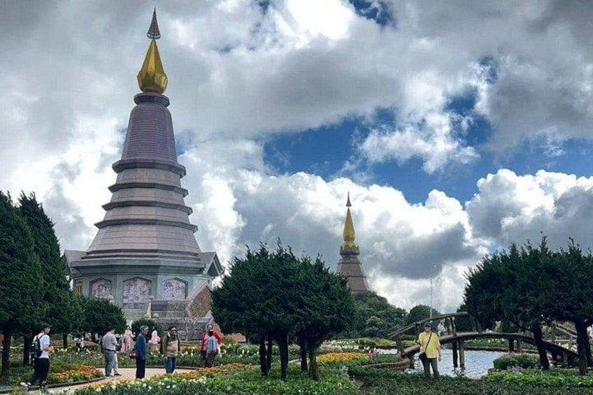 A large stupa with a golden spire, surrounded by trees and a pond with people around. 5