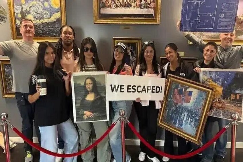 Eine Gruppe von Personen hält gerahmte Kunstwerke und ein Schild mit der Aufschrift 'WE ESCAPED!' in einem Museum. 2