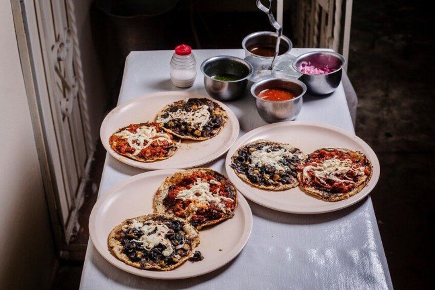 Five pizzas on plates with various toppings, accompanied by condiments in metal containers. 1