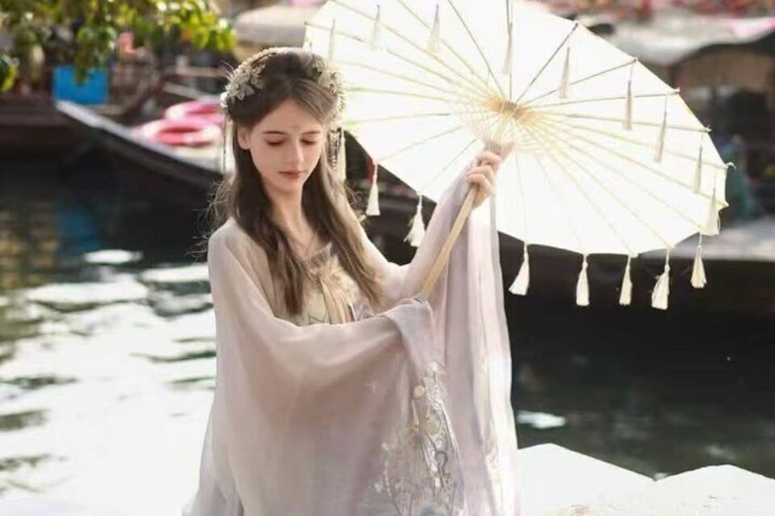A person holding a white parasol by a body of water with boats in the background. 2