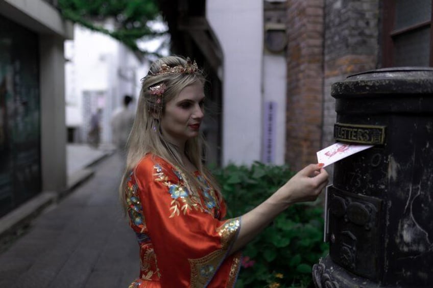 A person in a red dress with floral patterns standing next to a mailbox. 3