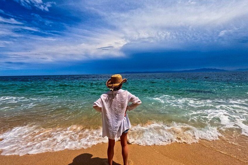 A person standing on a sandy beach facing the ocean, wearing a straw hat and a light-colored shirt. 2