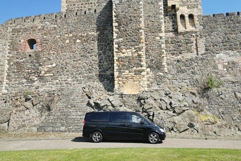Eine steinerne Burgmauer mit einem schwarzen Auto davor. 4