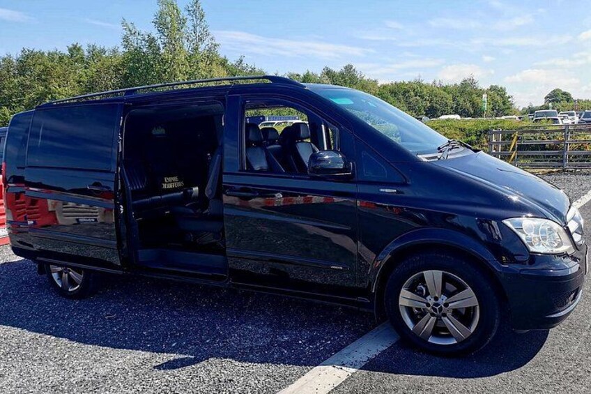 Ein schwarzer Van steht auf einem Parkplatz mit Bäumen und einem Zaun im Hintergrund. 5