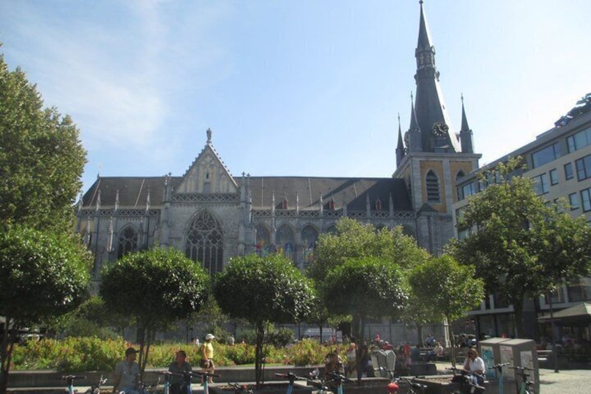 A historic cathedral with a tall spire, surrounded by trees and benches in a public square. 1