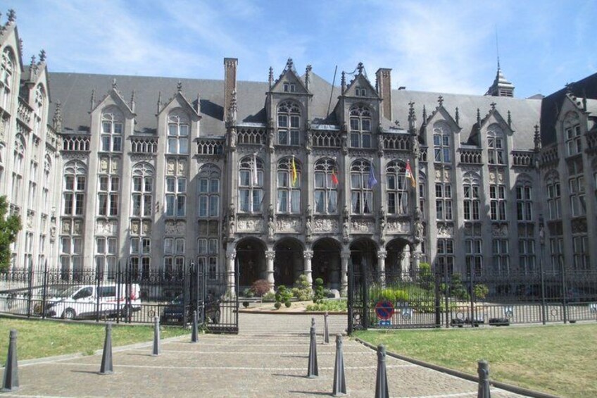 A large, historic building with intricate architecture, a paved courtyard, and a clear sky. 3