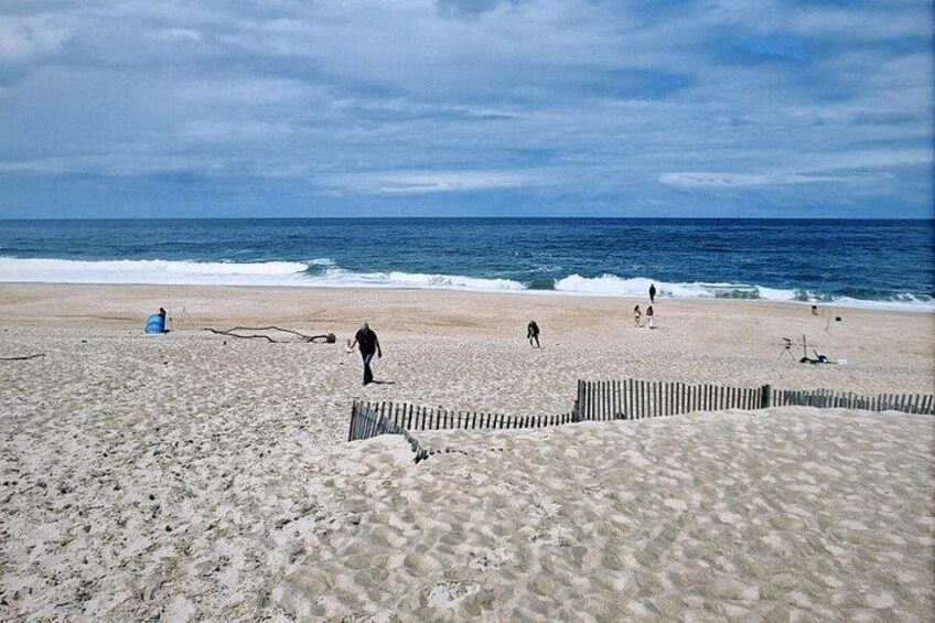 Una playa arenosa con una cerca de madera, olas del océano y algunas personas caminando. 3