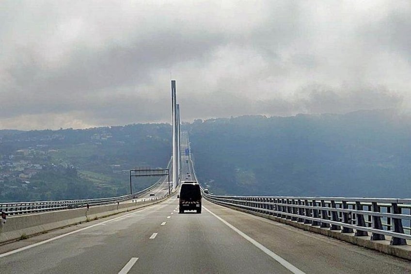 A bridge with a central tower, a road with vehicles, and a hilly landscape in the background. 2