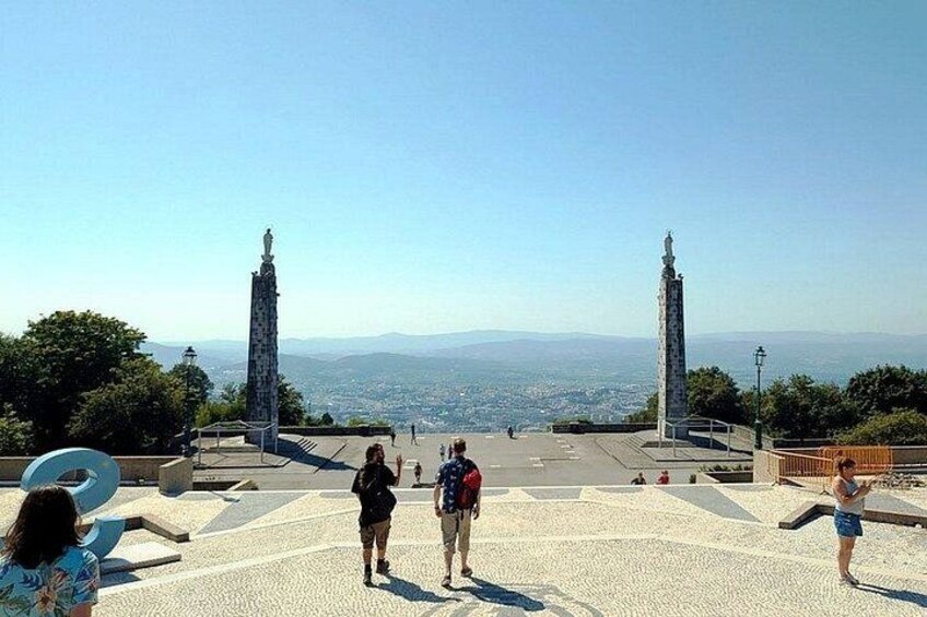 A paved area with two tall monuments, a clear sky, and distant cityscape. 4