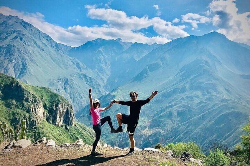 Two people performing a yoga pose on a mountain peak with a view of a valley and mountains in the background. 4