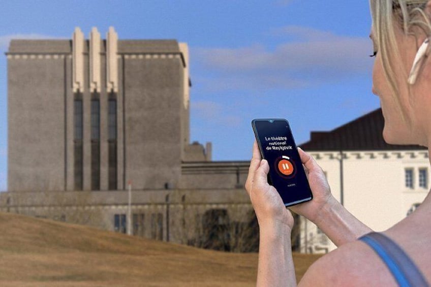 En person holder en smartphone med en teaterapp, stående foran en stor bygning med et unikt arkitektonisk design. 4