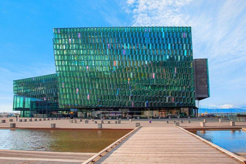 Un edificio moderno in vetro con facciata riflettente, un molo di legno che conduce all'acqua e un cielo azzurro limpido. 2
