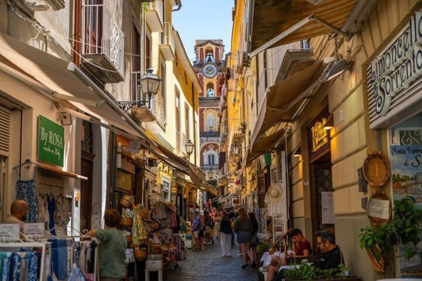 A narrow street with shops and a clock tower. 2