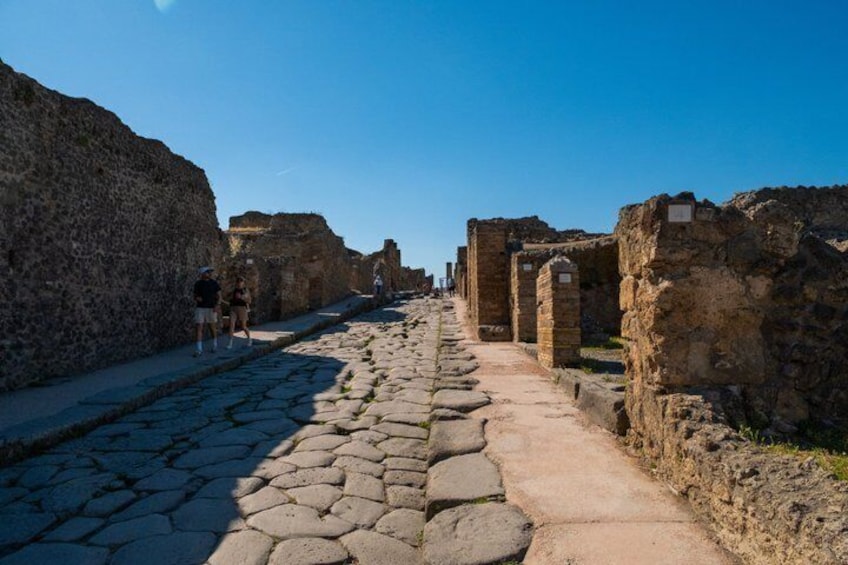 A cobblestone street flanked by ancient stone walls and ruins. 3