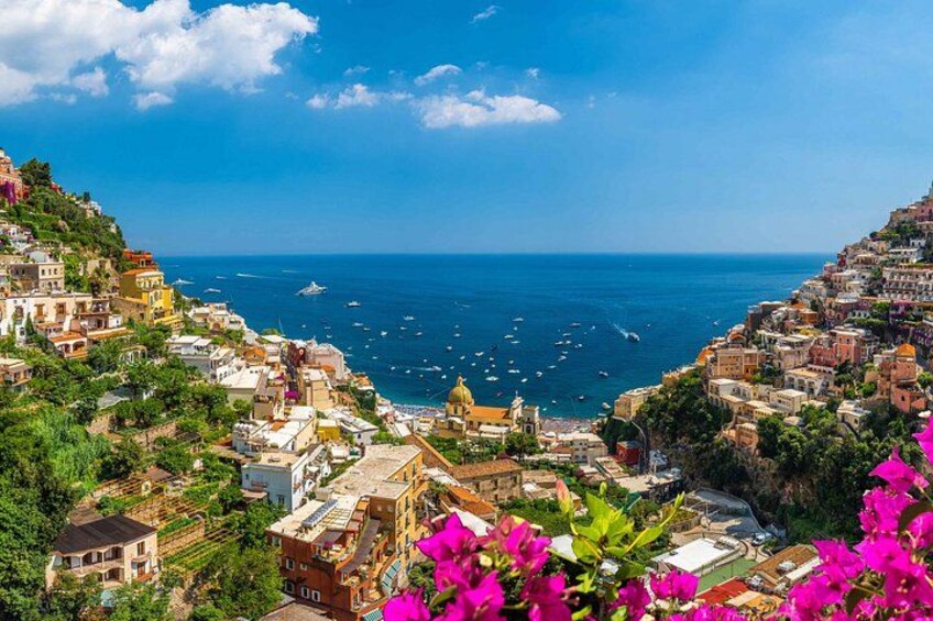 A coastal town with buildings on a hillside, a clear blue sky, and the sea with boats. 2