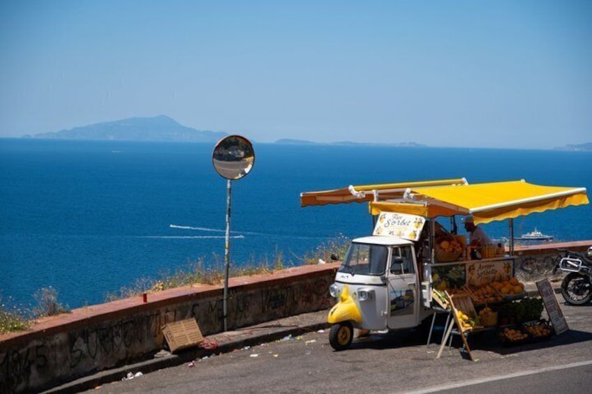 A food cart by the roadside with a view of the sea and mountains in the background. 5
